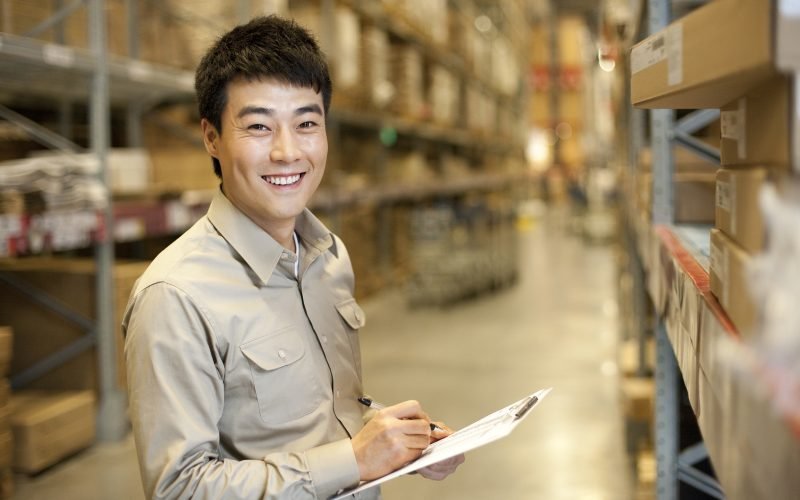 Female Chinese warehouse worker with clipboard and walkie-talke